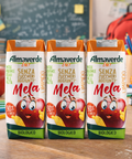 Three boxes of Almaverde Mela juice with cartoon apple characters on a school desk background.